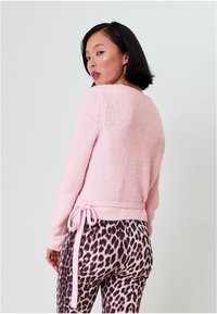 Helles Rosa, weicher, gestrickter Pullover mit langen Ärmeln und einem Bindeband in der Taille. Kombiniert mit figurbetonten Leggings im Leopardenmuster mit glänzender Textur.