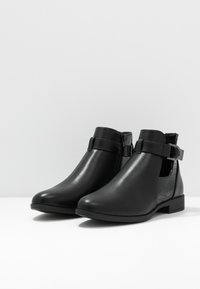 Bottines noires en cuir lisse avec un panneau à texture crocodile, dotées d'une fermeture éclair latérale et d'un talon plat.