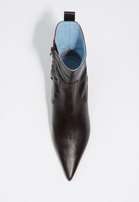 Botín de tobillo de punta afilada hecho de cuero marrón oscuro con un suave forro interior azul y una lengüeta trasera para facilitar el calzado.