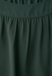Tejido verde oscuro con una textura suave, que presenta pliegues fruncidos en la cinturilla. El material parece ligero y transpirable.