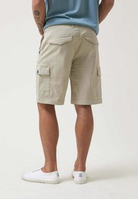 Pantalones cortos cargo beige con dos bolsillos laterales y bolsillos traseros, fabricados con una tela de textura suave. Diseñados para un ajuste relajado, de longitud hasta la rodilla.