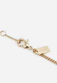 Gold chain with a lobster clasp, featuring a small pendant tag engraved with "COACH." Smooth metal texture, elegant link design.