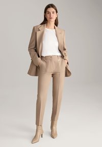 Beige blazer and matching tapered trousers made of smooth fabric. Underneath, a white shirt. Beige pointed ankle boots with a sleek design.