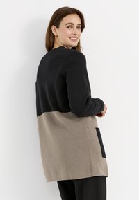 Strickjacke in Schwarz und Beige mit einem Farbkombinationsdesign, langen Ärmeln und einer Seiten Tasche. Weiche Textur und entspannter Schnitt.