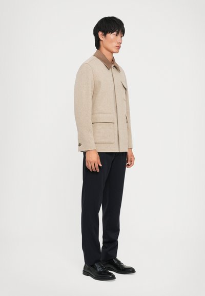 Beige villasegu segu jacket pruunist kaelusest, esiosa nupu sulgemise ja kahe esikoti välimusega. Kandsid tumedaid pükse ja musti kingi.