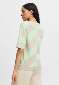 Kurze Ärmel Strickpullover mit geometrischem Muster in Hellgrün und Beige. Gerippter Saum und Bündchen mit Streifen. Weiche Textur.