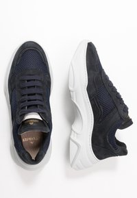 Sneaker blu navy in rete e suede con suole bianche spesse, una scarpa vista dall'alto, l'altra di lato.