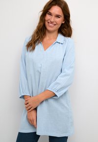Tunica azzurro chiaro con scollatura a V e collo senza bottoni. Presenta maniche 3/4 elasticizzate e una vestibilità ampia e fluida. Tessuto morbido.