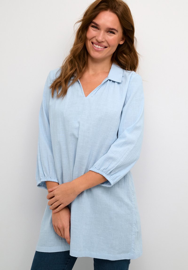 Tunica azzurro chiaro con scollatura a V e collo senza bottoni. Presenta maniche 3/4 elasticizzate e una vestibilità ampia e fluida. Tessuto morbido.