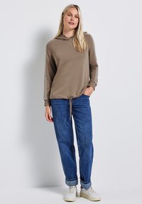 Felpa con cappuccio color marrone chiaro, caratterizzata da righe laterali e orlo con lacci. Abbinata a jeans blu a vestibilità ampia e sneakers bianche.
