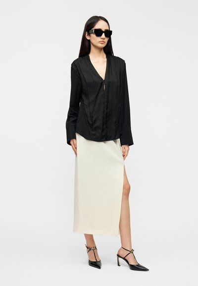 Μαύρο σατέν μπλουζάκι με V-λαιμόκοψη και ρυτιδωτές λεπτομέρειες, συνδυασμένο με εκρού σατέν μακρύ φούστα με σφηκοφωλιά στο πλάι. Φορεμένο με μαύρες γόβες στιλέτο.