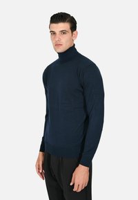 Maglione a collo alto blu navy in un tessuto a maglia liscia, design aderente, con polsini e orlo a costine, abbinato a pantaloni neri.