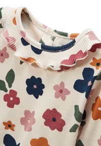 Blouse côtelée avec une base crème, ornée de motifs floraux multicolores en rose, bleu, orange et vert. Encolure froncée avec un bouton de fermeture.