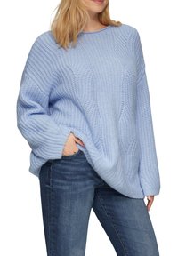 Helles, blaues Strickpullover mit lockerer Passform, gerippter Textur und weiten Ärmeln. Kombiniert mit dunkelblauen Jeans. Hat einen runden Halsausschnitt.