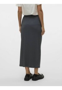Jupe longue grise texturée avec un design plissé, associée à des chaussures à plateforme noires. La jupe a une taille haute et tombe jusqu'aux mollets.