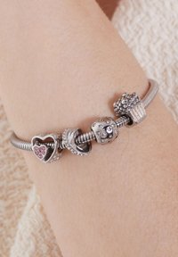 Zilveren armband met bedels: een hart met roze stenen, een gedraaide ontwerp, een ster-patroon kraal, en een cupcake-bedel.