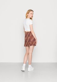 T-shirt branca curta combinada com uma saia castanha com padrão, apresentando uma bainha com folhos e uma mistura de designs geométricos e com pontos.