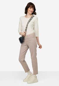 Lichtgekleurde, langmouwige top; beige, taps toelopende broek met een elastische tailleband; witte chunky sneakers; kleine zwarte schoudertas met een patroon op de band.