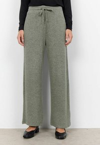 Grau-grüne, weit geschnittene Hose mit Tunnelzugbund, aus weichem, strukturiertem Stoff. Kombiniert mit schwarzen flachen Schuhen.