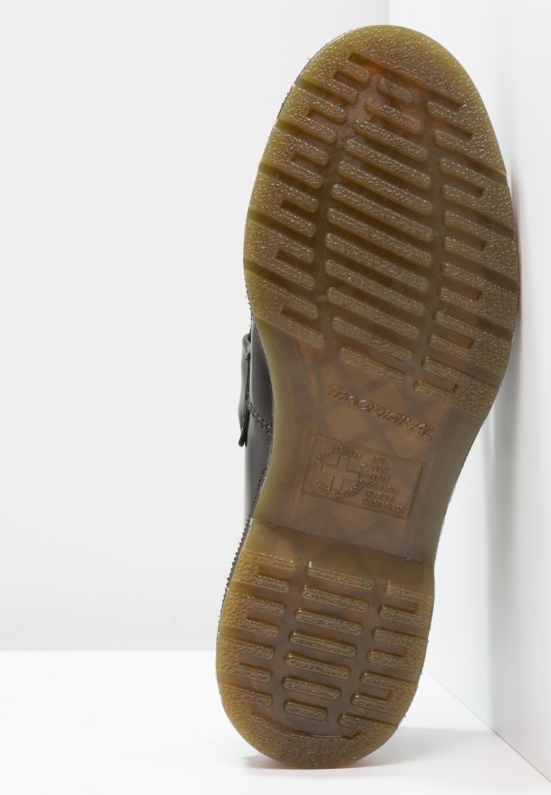 Scarpa nera in pelle con una suola testurizzata, caratterizzata da un motivo di tassellatura pronunciato e un logo impresso sulla parte inferiore. Finitura liscia.