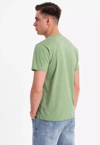 Grøn kortærmet t-shirt med en stiplet mønster, rund halsudskæring og blød tekstur. Båret sammen med lyseblå slidte jeans.