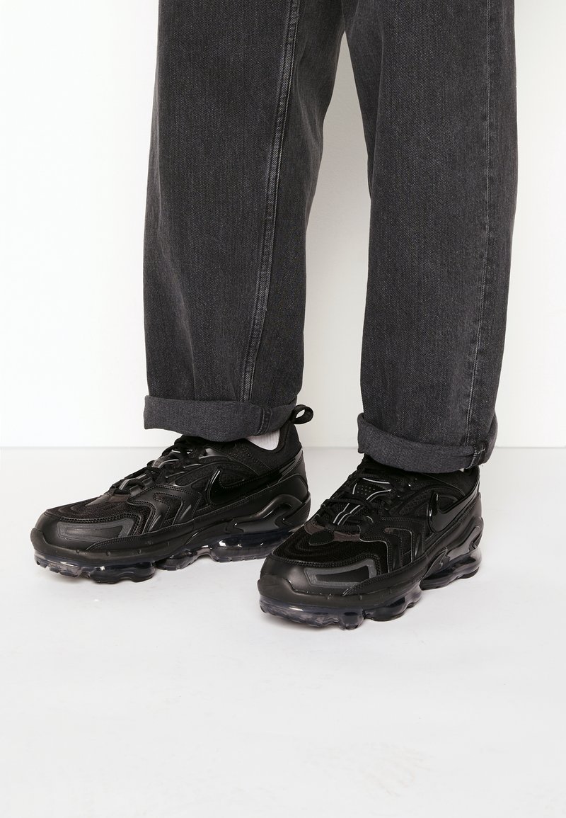 Černé tenisky Nike mají vlnitý design, síťovaný svršek a průhlednou podrážku. Nosit je s ohrnutými tmavě šedými džínami.