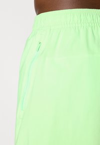 Shorts de sport vert fluo avec une taille élastique et une poche zippée sur le côté. Texture lisse, matériau léger et design simple.