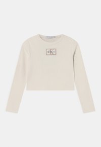 Top corto a maniche lunghe color beige chiaro realizzato in tessuto a coste, con un'etichetta logo rettangolare con "Calvin Klein Jeans" e dettagli "K".