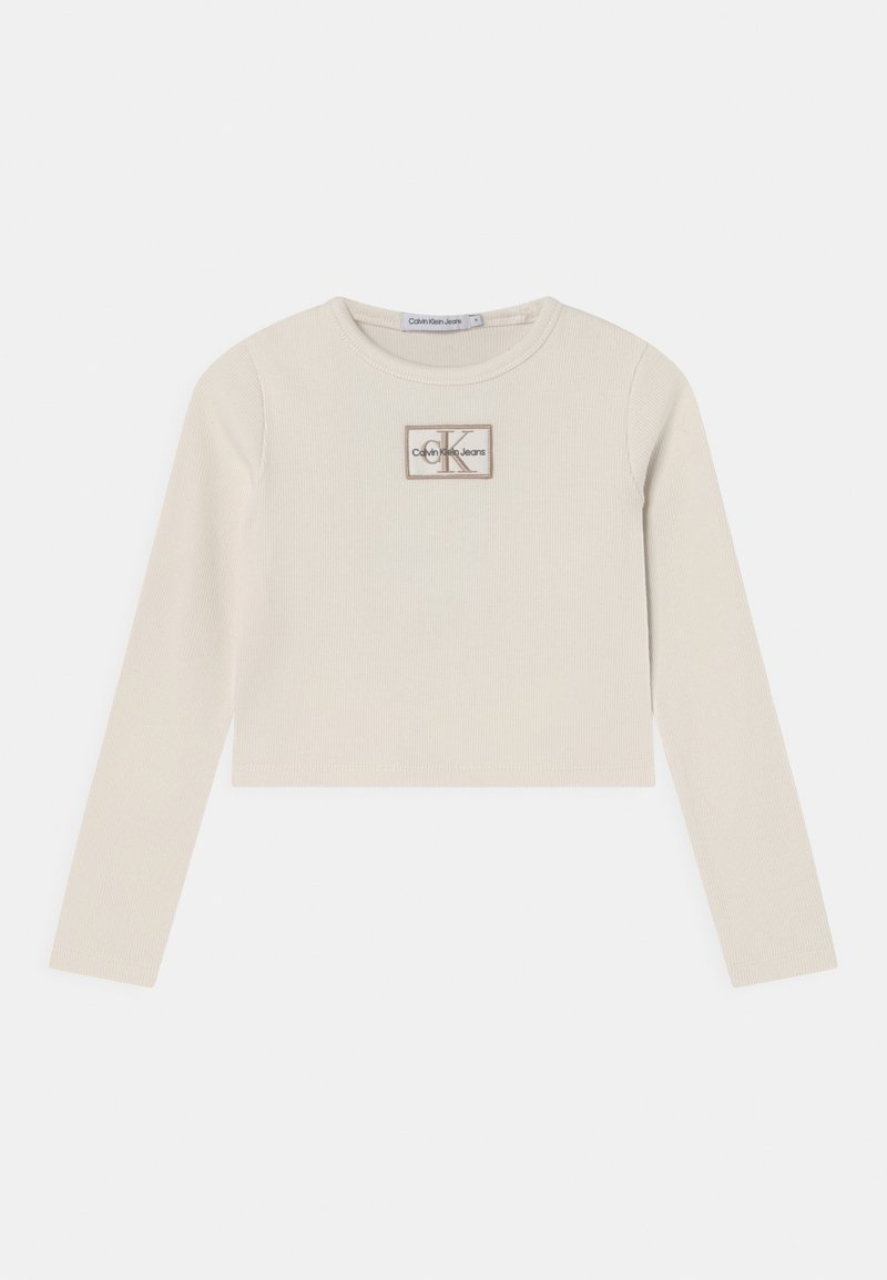 Top corto a maniche lunghe color beige chiaro realizzato in tessuto a coste, con un'etichetta logo rettangolare con "Calvin Klein Jeans" e dettagli "K".