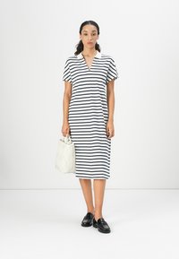 Stripet midi-kjole med V-hals, korte ermer og løs passform. Hvit og marineblå striper, kombinert med en teksturert hvit håndveske og svarte sko.