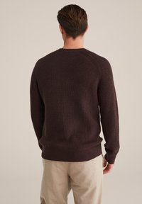 Brūns teksturēts adījuma džemperis ar apaļu dekoltē un ribotām piedurknēm, ar raglāna piedurknēm un pieguļošu jostas daļu.