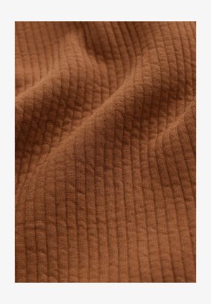 Ruskean kankaan ribbikuvio pehmeällä pinnalla, jossa on hienovarainen pystyratkaisu ja luonnonkuituja lisäämään syvyyttä ja visuaalista kiinnostavuutta.