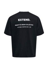 T-shirt oversize nera con testo bianco sul retro: "ESTENDI." e "COLLEZIONE PRONTA DA INDOSSARE AUTUNNO / INVERNO 2025 - 2026."