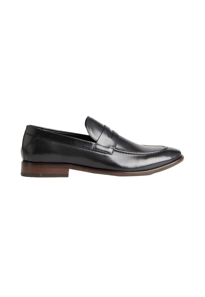 Mocasín de cuero negro con un acabado suave, una costura ligeramente elevada a lo largo del frente y un bajo tacón de madera apilada.