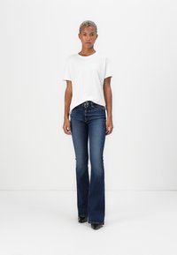 Witte korte mouwen t-shirt gepaard met donkerblauwe flared jeans, met een lichte glans, subtiele stiksels en zwarte hakken.