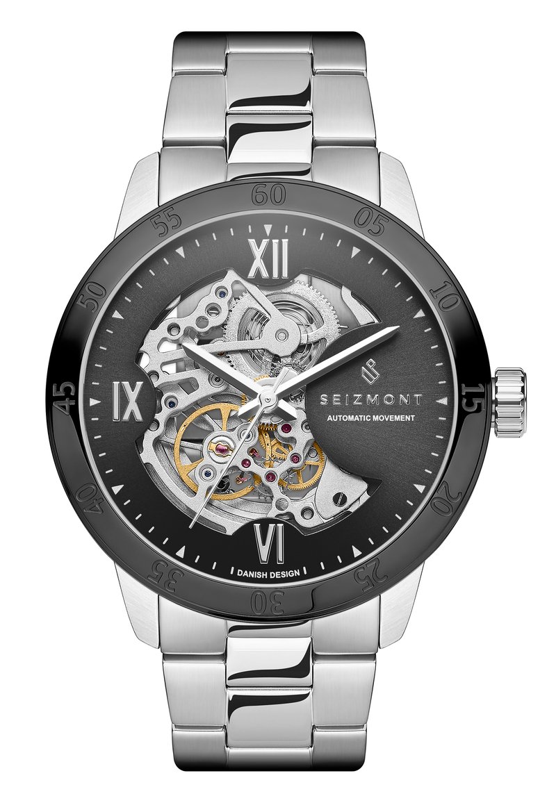 Herreklokke med gjennomsiktig mekanisk urverk; armbånd i rustfritt stål; svart skive med romerske tall; sølvaksenter og gullgir.