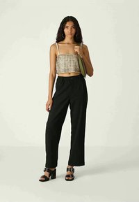 Ljusbrun rutigt crop top, högmidjade svarta byxor och svarta klacksandaler. Modellen bär en olivgrön väska.