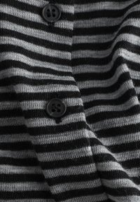 Gros plan sur un tissu tricoté rayé noir et gris avec deux boutons noirs cousus dessus.