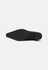 Semelle de chaussure noire présentant un design plat, des motifs de prise texturés, et un bout légèrement pointu avec des bords lisses et des accents matériels minimalistes.