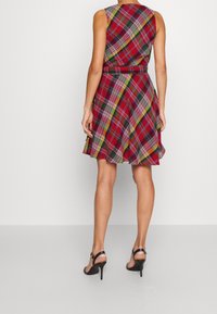 Červené kostkované šaty s přiléhavým korzetem a rozšířenou sukní. Mají vypasovaný pas a bezramenný design. Noseny s černými podpatky.