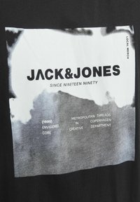 Černé bavlněné tričko s bílým grafickým potiskem. Text zahrnuje "JACK&JONES," "SINCE NINETEEN NINETY" a další designové prvky.