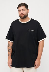 Zwarte katoenen T-shirt met korte mouwen en crèmekleurige manchetten, een ronde hals en witte geborduurde tekst op de borst.