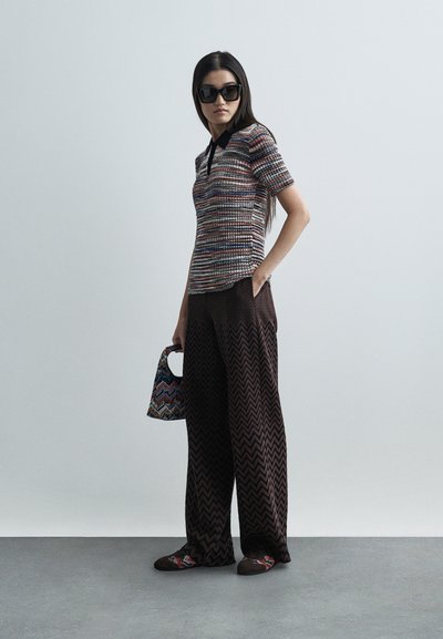 Polo en tricot avec un motif multicolore et un col noir, associé à un pantalon à large jambe à motifs chevrons marron et un sac à main graphique.
