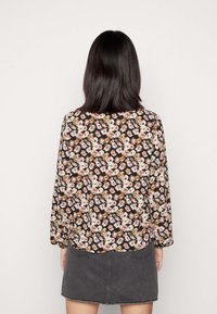 Blusa com padrão floral em fundo preto, mangas longas, corte solto e tecido macio. Combinada com uma saia de ganga cinza.