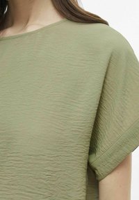 Maglietta in tessuto verde oliva con effetto rugoso, maniche corte e scollo arrotondato, con una texture morbida e dettagli di cuciture minimi.