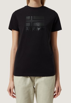 Czarny krótki rękaw t-shirt z błyszczącą czarną prostokątną flagą i napisem "NAPAPIJRI geographic" na piersi, noszony z jasnobeżowymi spodniami.