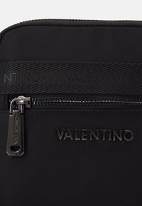 Borsa nera in nylon con tracolla texturizzata con marchio "VALENTINO", cerniera con accessori argentati e logo in rilievo sulla parte anteriore.