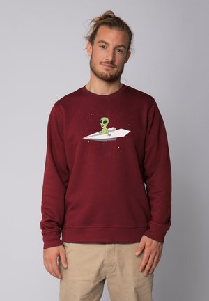 Bordeauxfarbener Pullover aus weichem Material mit einem grünen Alien-Graphic auf einem Papierflieger, mit rundem Halsausschnitt und gerippten Bündchen.