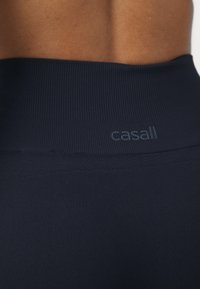 Leggings atléticos azul marinho feitos de tecido canelado, com uma cintura lisa. Apresenta um logótipo discreto, Casall, próximo ao topo.