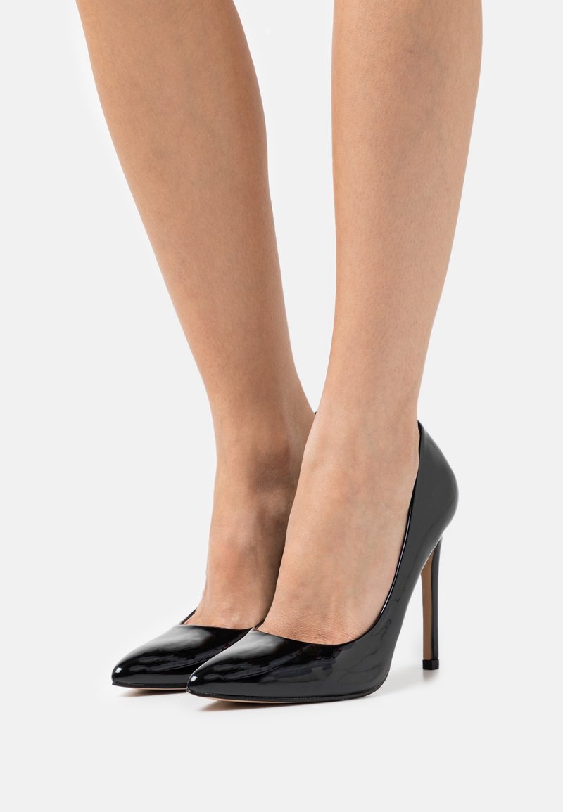 Escarpins en cuir verni noir avec bout pointu et talon stiletto fin. Texture lisse et design élégant.